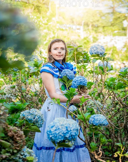 Young Nicaraguan woman in traditional folk costume holding flowers in the field. Portrait of beautiful woman in national folk costume in a field of flowers. Nicaraguan national folk costume