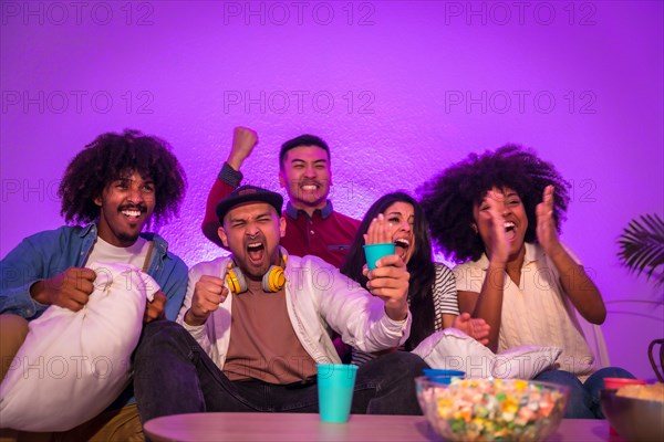 Adult party. Young people sitting on the sofa watching a football game with popcorn. Emotion for soccer