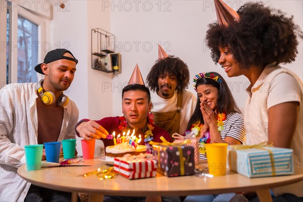 Multi-ethnic group of friends at a birthday party on the sofa at home with a cake and gifts