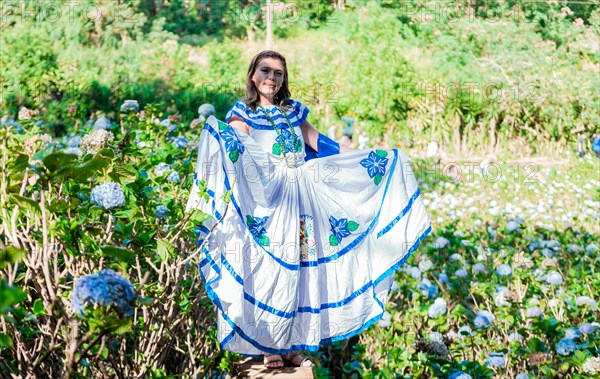 Smiling woman in national folk costume in a field surrounded by flowers. People in Nicaraguan national folk costume. Young Nicaraguan woman in traditional folk costume in a field of Milflores