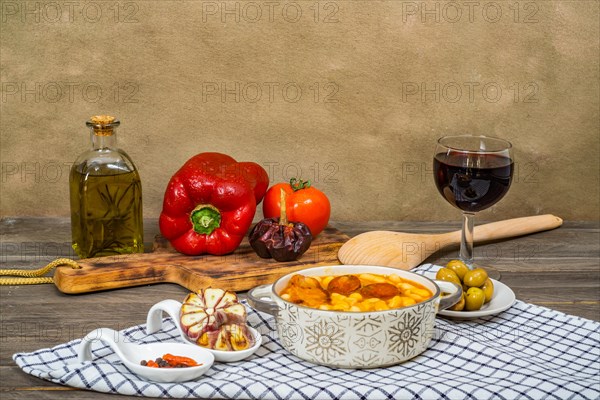 White beans stewed with bacon and chorizo in a ceramic pot on a wooden table with all the ingredients of the recipe