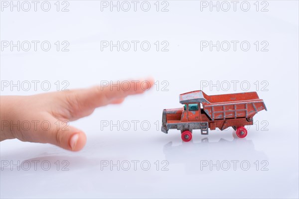 Baby hand is about to grab a red toy truck on white background