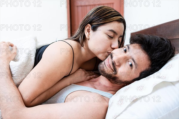 Woman in bed kissing her husband on the forehead. Wife in bed kissing husband on the forehead