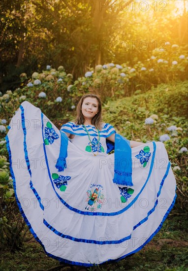 Smiling girl in national folk costume in a field surrounded by flowers