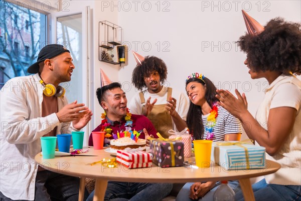 Multi-ethnic group of friends at a birthday party on the sofa at home with a cake and gifts