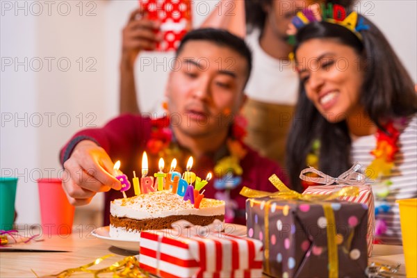 Multi-ethnic group of friends at a birthday party on the sofa at home with a cake and gifts