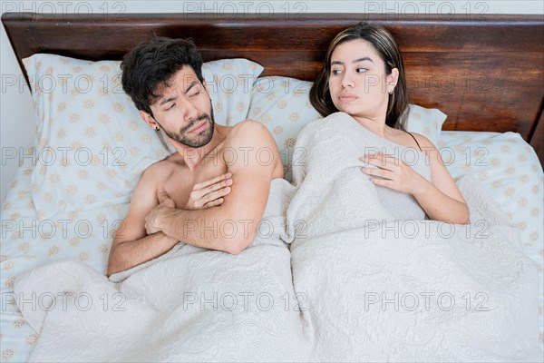 Upset couple in bed with crossed arms. Woman lying in bed upset with her husband. Angry man and woman in bed with crossed arms. Marriage problems concept