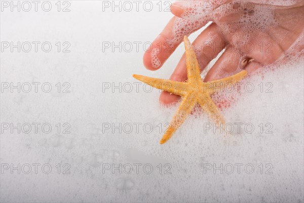 Hand holding starfish in water covered with foam