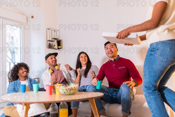 Group of multi-ethnic friends on a sofa eating pizza and drinking soft drinks at a home party