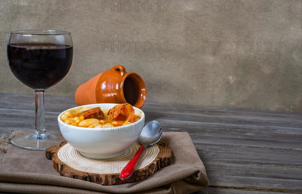 White beans stewed with chorizo in white ceramic bowl on wooden table with a glass of red wine