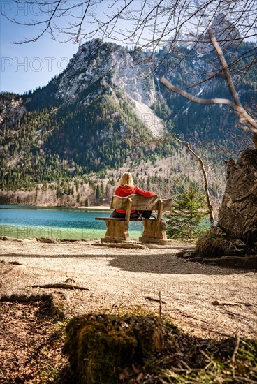 Woman sitting on bench and looking at the lake and the mountains