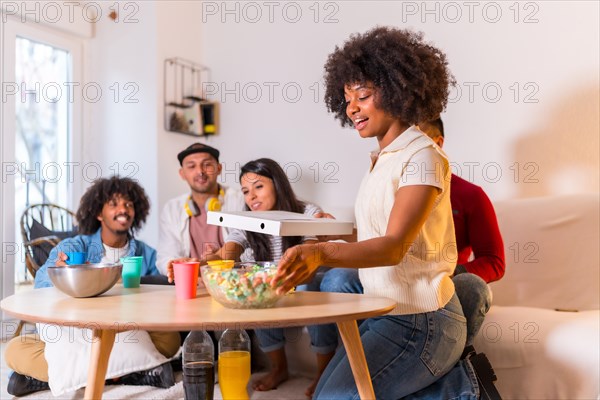 Group of multi-ethnic friends on a sofa eating pizza and drinking soft drinks at a home party