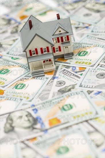 Small model house on layer of one hundred dollar bills