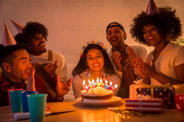 Multi-ethnic group of friends at a birthday party on the sofa at home with a cake and gifts