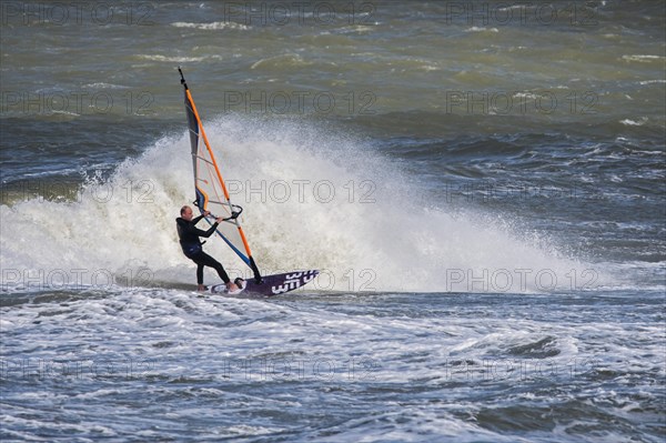 Recreational windsurfer in black wetsuit practising classic windsurfing along the North Sea coast in windy weather during winter storm