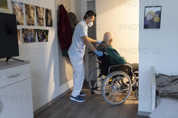 Geriatric nurse pushing a wheelchair through a door in a nursing home