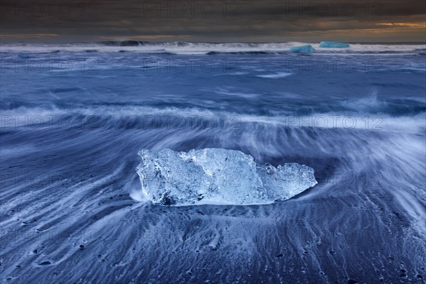 Melting block of ice washed on beach along the Atlantic Ocean coastline at Breidamerkursandur black sands in winter