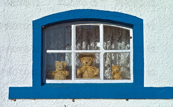 Three teddy bears made of straw behind a window