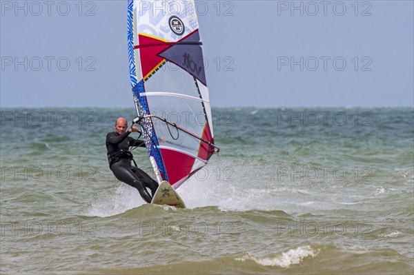 Recreational windsurfer in black wetsuit practising classic windsurfing along the North Sea coast