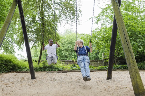 Temporary grandparents. Grandfather swinging with his charge in a playground.