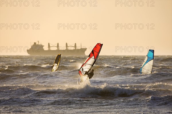 Ship and three windsurfers windsurfing on the North Sea at sunset
