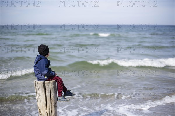 Symbolic photo on the theme of loneliness in childhood. A child sits alone on a wooden post by the sea. Arenshoop