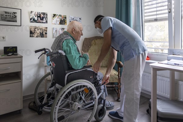 Carer helps old man stand up in a nursing home