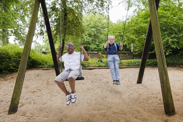 Temporary grandparents. Grandfather swinging with his charge in a playground.