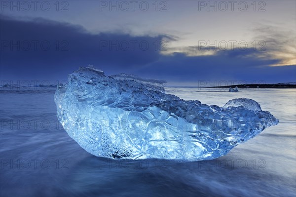 Melting block of ice washed on beach along the Atlantic Ocean coastline at Breidamerkursandur black sands in winter