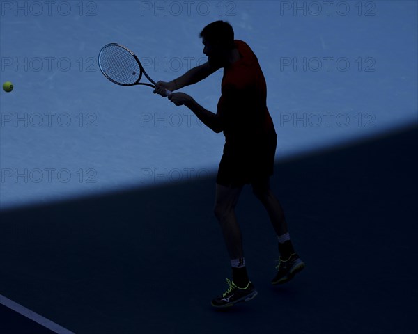 Silhouette of German tennis player Mats Moraing hitting a backhand during the Australian Open 2022 tennis tournament