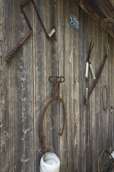 Assorted antique manual tools displayed on side wall of wood plank storage shed