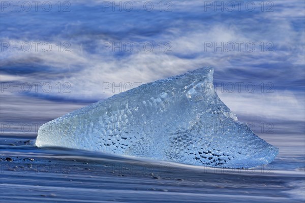 Melting block of ice washed on beach along the Atlantic Ocean coastline at Breidamerkursandur black sands in winter