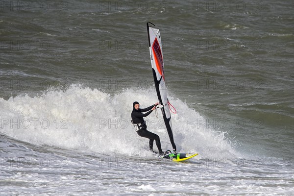 Recreational windsurfer in black wetsuit practising classic windsurfing along the North Sea coast in windy weather during winter storm