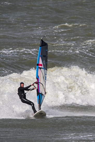 Recreational windsurfer in black wetsuit practising classic windsurfing along the North Sea coast in windy weather during winter storm