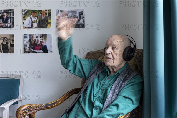 Old man in nursing home conducts to music