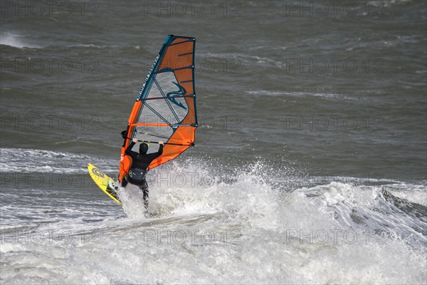 Recreational windsurfer in black wetsuit practising classic windsurfing along the North Sea coast in windy weather during winter storm