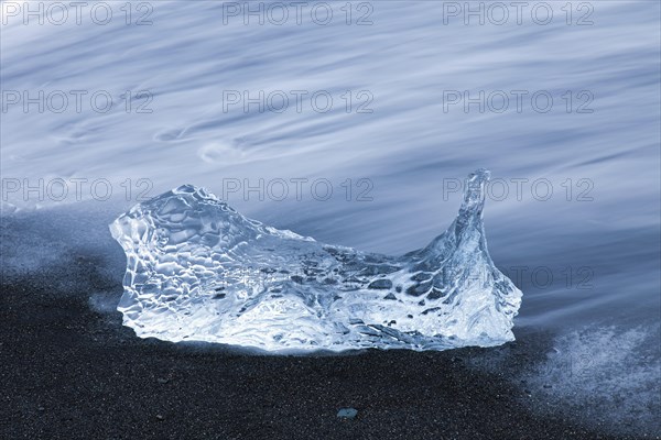 Melting block of ice washed on beach along the Atlantic Ocean coastline at Breidamerkursandur black sands in winter