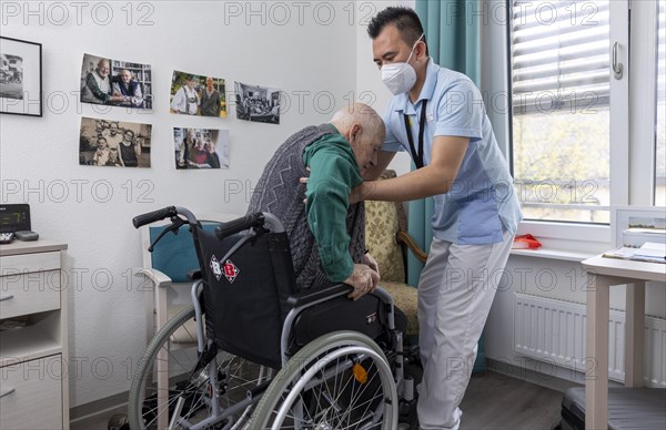 Carer helps old man stand up in a nursing home