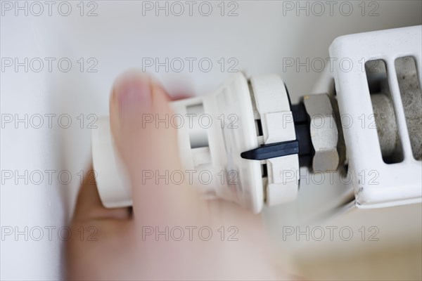 Symbolic photo on the subject of increased heating costs. A person turns the thermostat of a heating system. To save on heating costs