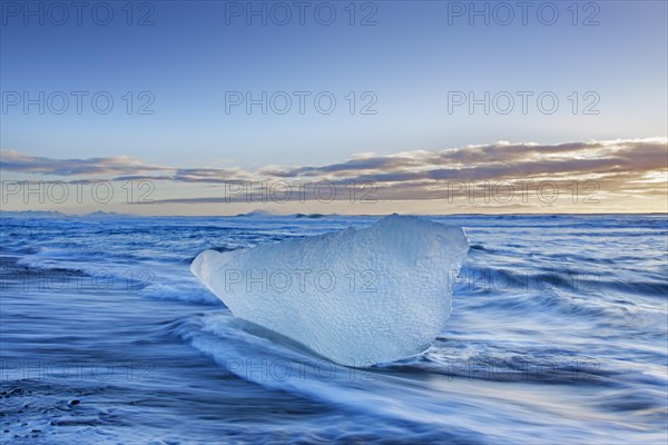 Melting block of ice washed on beach along the Atlantic Ocean coastline at Breidamerkursandur black sands in winter