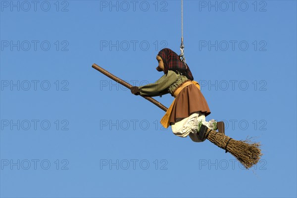 A witch doll on a broomstick hangs in the air and a blue sky in the background