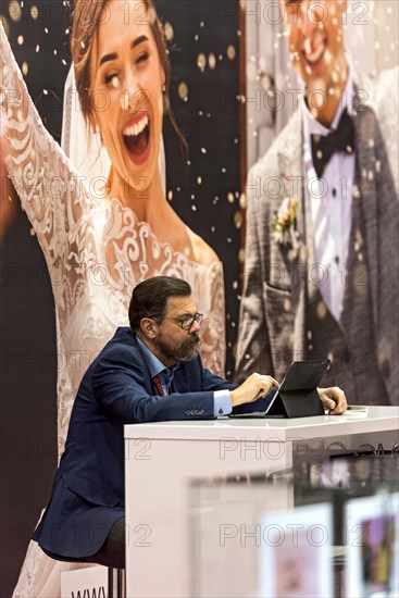 Businessman with tablet computer in front of photo wall with wedding couple