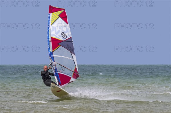 Recreational windsurfer in black wetsuit practising classic windsurfing along the North Sea coast
