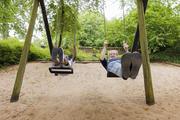 Temporary grandparents. Grandfather swinging with his charge in a playground.