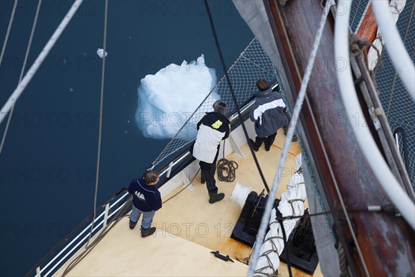 Sailing ship passing melting iceberg floating in ocean near Svalbard