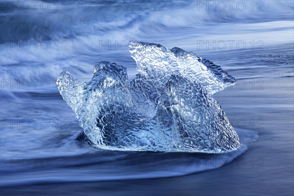 Melting block of ice washed on beach along the Atlantic Ocean coastline at Breidamerkursandur black sands in winter