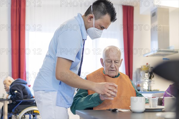 Carer helps a man to drink in a nursing home