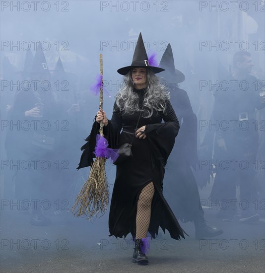 A witch in black and with a broom and behind everything in the smoky mist at the carnival in the city of Rijeka