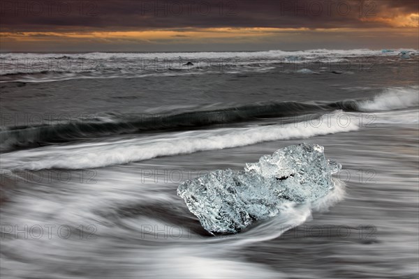 Melting block of ice washed on beach along the Atlantic Ocean coastline at Breidamerkursandur black sands in winter