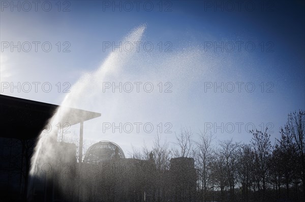 A water sprinkler waters a meadow in front of the Reichstag in the morning. Berlin